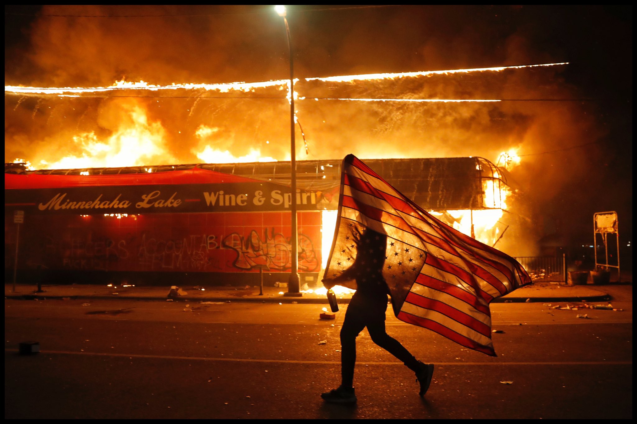 A protester carries a U.S. flag upside-down, a sign of distress, next to a burning building Thursday, May 28, 2020, in Minneapolis. Protests over the death of George Floyd, a black man who died in police custody Monday, broke out in Minneapolis for a third straight night.
